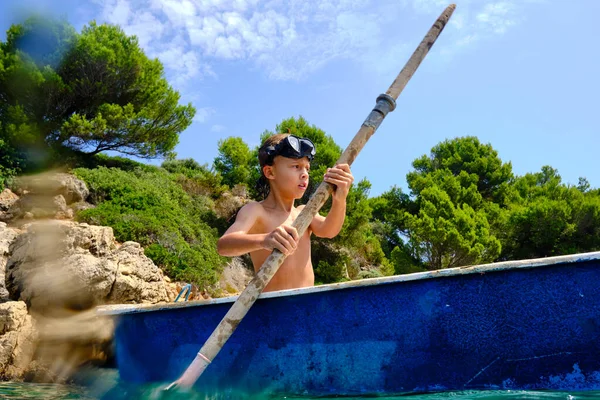 在热带旅游胜地的夏季旅行中 身穿潜水面罩划船的男孩 带着桨在海面上与岩石海岸和树木擦肩而过 — 图库照片