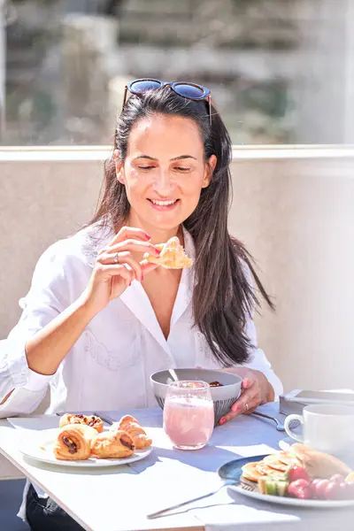 夏日早晨 一个快乐的女人在阳台吃早餐的时候 一边吃粥一边吃着美味的羊角面包 — 图库照片