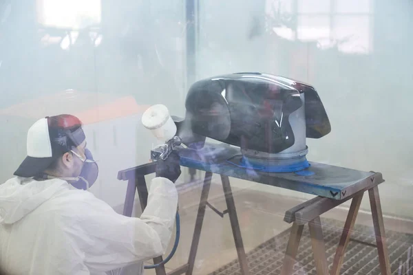 保護ユニフォームと呼吸器で匿名の男性技術者のガラスバックビューを通して 隔離された部屋の空気スプレーヤーが付いているオートバイの燃料タンクを塗ります — ストック写真