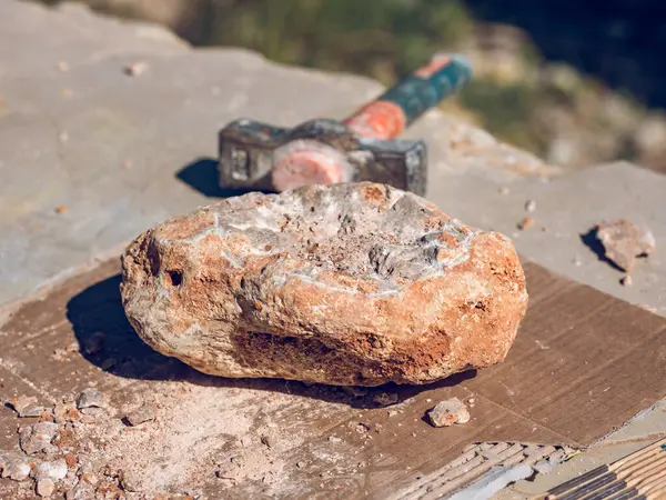 日光の石工場のテーブルの上のハンマーの近くの浜辺の表面に置かれた粗い岩の上から — ストック写真