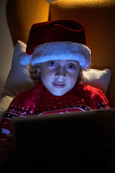 Симпатичный Маленький Мальчик Рождественской Шляпе Свитере Помощью Планшета Сидя Уютном — стоковое фото