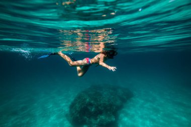 Yüzgeçli ve şnorkelli derin mavi deniz suyunda yüzen anonim bir gencin yan görüntüsü.