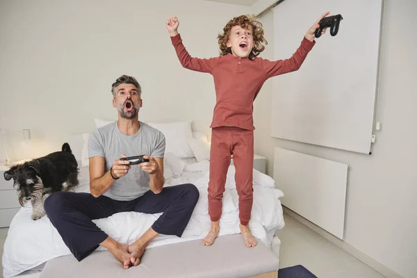Полная Длина Эмоционального Мужчины Веселый Прыгающий Ребенок Играющий Видеоигру Вместе — стоковое фото