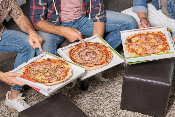 リビングルームに座ってさまざまな種類のピザを指すカジュアルな服で匿名の男性の友人を収穫の上から — ストック写真