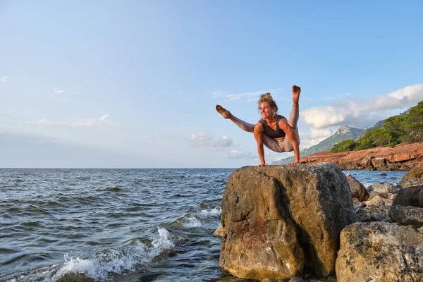 身穿运动服 面带微笑的女运动员 体态优美 体态匀称 在日落时练习瑜伽时欣赏波涛汹涌的大海 — 图库照片
