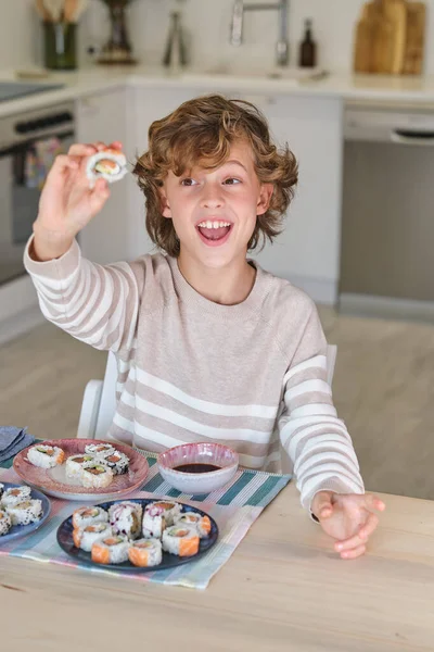Positieve Jongen Casual Kleding Tonen Sushi Naar Camera Terwijl Zitten — Stockfoto