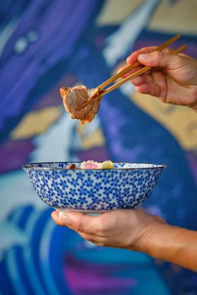 食欲をそそるチャーシュー肉を箸で持ちながら ラーメンのスープに鳴滝を乗せて食べる匿名の人をクロップ — ストック写真