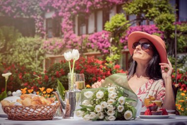 Mutlu bir kadının güneşlenirken ve bahçede kahvaltı ederken çekilmiş fotoğrafı..