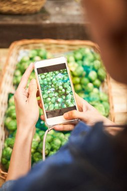 Markette sepette enginar yığını fotoğrafı çeken, cep telefonlu tanınmayan bir şahsın tepesinden.