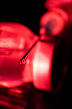 Kırmızı ışıkta siyah arkaplana karşı cam şişeye yerleştirilen iğnenin ucundaki aşı damlasına odaklan