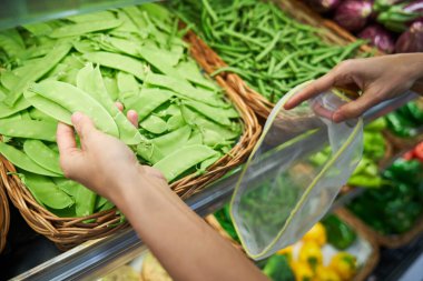 Plastik kabı olan isimsiz müşterinin yukarısından süpermarketteki raflardaki sepetlerden olgun bezelye kabuklarını seçiyor.