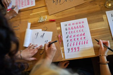 İsimsiz bayanların kağıt üzerine kalem ve fırçayla alfabe harfleri yazışlarının en üst görüntüsü