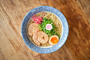 Lezzetli ramen çorbası haşlanmış yumurta ve ahşap masaya yerleştirilmiş seramik kasede servis edilen chashu domuz eti.