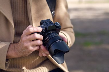 Bej ceketli tanınmayan bir adam profesyonel fotoğraf makinesinden fotoğraflara bakıyor ve hafta sonunu doğada geçiriyor.