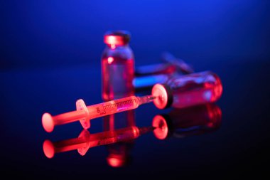 Şırınganın yakın plan görüntüsü tıbbi şişeye yerleştirildi ve neon ışıkta yansıtıcı yüzeye yerleştirilen COVID19 aşısıyla dolduruldu.