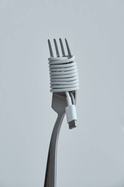 Beyaz kulaklıklar çelik çatala spagetti gibi dolanmış gri arka planda veri tüketimi kavramını temsil ediyor.