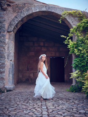 Uzun saçlı, dantelli gelinlik giyen, antik taş evin kemerli girişinin yanında duran çekici bir ergen vücudu.