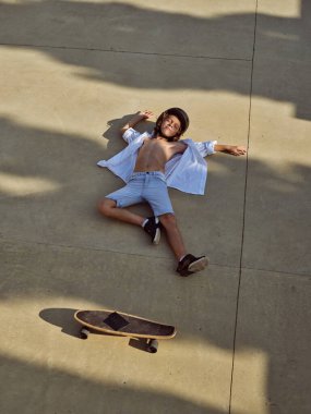 Yüksek açılı, kasklı, düşmüş bir çocuk güneşli bir yaz gününde uzun tahtasıyla yatıyor.