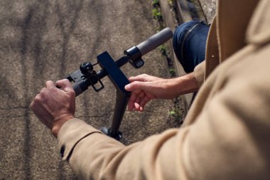 Güneşli bir günde parkta asfalt yolda dikilirken elektrikli scooter kullanan isimsiz bir erkek.