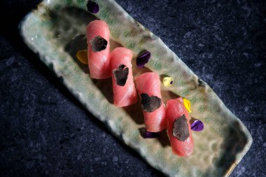 Uzatılmış tabağın tepesinde loş ışıkta yer mantarlarıyla süslenmiş ton balığından yapılmış suşi seti var.