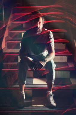 Ciddi sakallı, sıradan giyinmiş, karanlık bir gece kulübünde uzun metrajlı bir gece kulübünde kameraya bakan bir adam.