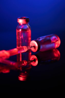 Karanlık odadaki yansıtıcı yüzeye yerleştirilmiş COVID aşısıyla dolu tıbbi şırınga ve ampuller.