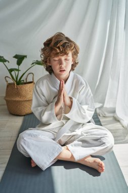 Beyaz kimonolu bir çocuğun vücudu yoga minderinde kapalı gözlerle oturmuş namaste elleriyle Padmasana çalışırken meditasyon yapıyor.