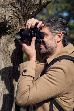 Sırt çantalı erkek fotoğrafçı, güneşli havada yeşil ormanı keşfederken profesyonel fotoğraf makinesiyle fotoğraf çekiyor.