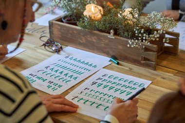 Atölyede kaligrafik yazım dersinde kağıt üzerine satır satır harfler yazan isimsiz kadın çizer