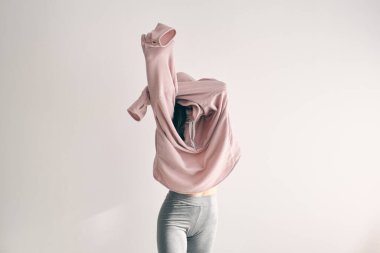 Beyaz duvarın önünde duran uzun kollu ve kollu süveterli tanınmayan bir kadın.