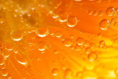 Şeffaf alkollü cin ve tonik karışımlı portakal diliminin tam kare görüntüsü. Işık odasında küçük yuvarlak kabarcıklar var.