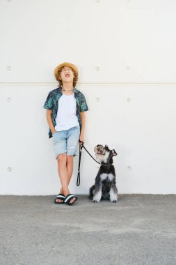 Moda kıyafetleri içinde, minyatür Schnauzer köpeğiyle duvarın önünde bağıran pozitif çocuklu bir vücut.