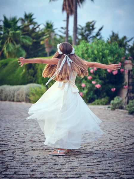 夏の庭の緑の木々の近くのパス上に回転白いドレスの認識できない屈託のない十代の少女のバックビュー — ストック写真