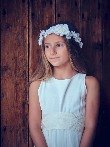 Serene Preteen子供で白いドレスと花の花輪見て離れて立っている間に木製の壁 — ストック写真