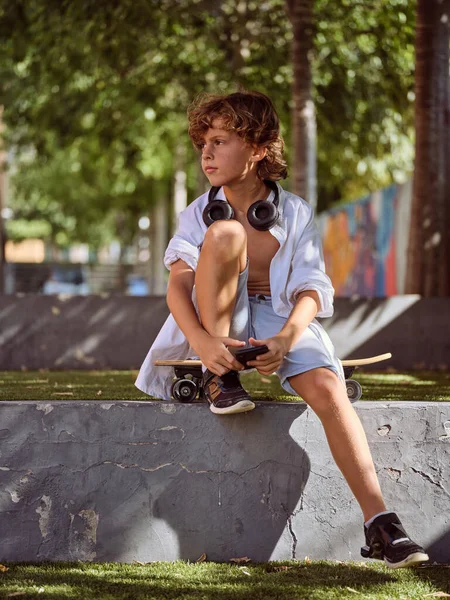 Cuerpo Completo Niño Preadolescente Sentado Monopatín Parque Con Auriculares Mientras —  Fotos de Stock