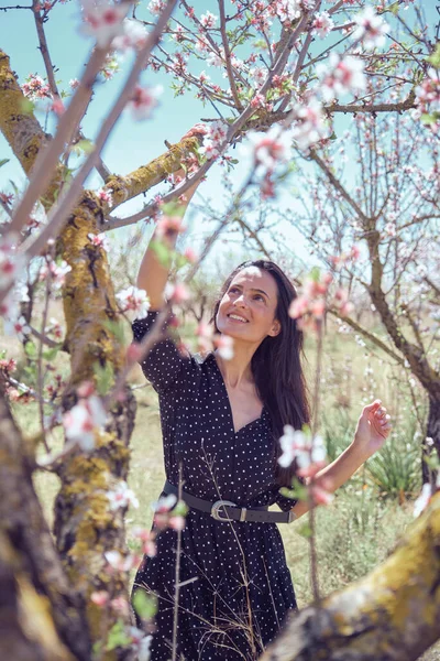 夏の日に葉と咲く花で覆われたツイッグとリンゴの木の下に立っているベルトドレスの魅力的な女性 — ストック写真