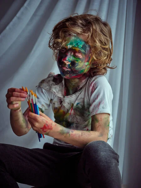 Злобный Мальчик Повседневной Одежде Покрытый Красочными Красками Осматривающий Набор Кистей — стоковое фото