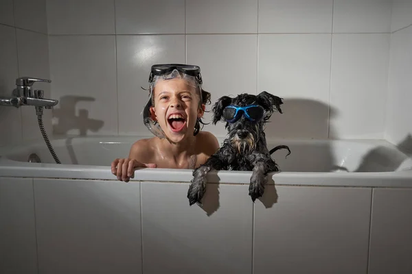 Dalgıç maskesi takmış, ağzı açık mutlu çocuk ve banyoda günlük hijyen rutini sırasında beyaz banyoda oturan tatlı köpek.