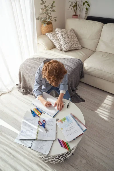 ソファに座ってカラフルな鉛筆でテーブルの上でスケッチしながら 自宅で居心地の良いリビングルームで休んでいる小さな男の子の高い角度 — ストック写真