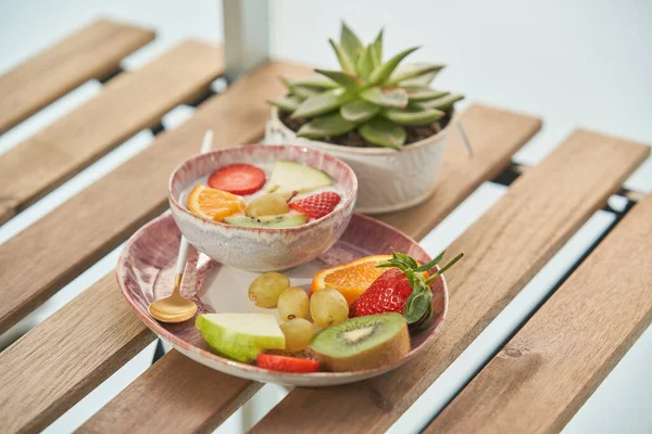 朝食時には軽めのキッチンに鉢植えの木のテーブルの上に新鮮な各種フルーツを乗せたおいしいヨーグルトトッピングのボウル — ストック写真