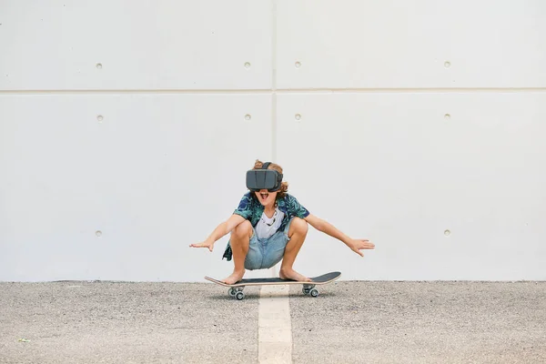 興奮した十代の男の子のフルボディでVrヘッドセットに乗るスケートボードと叫んで歩道で街の通り — ストック写真