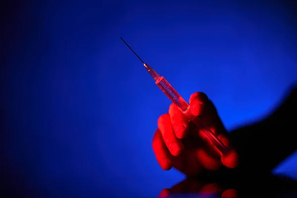 在深蓝色背景的暗室里用注射器扎针治疗无法辨认的病人 — 图库照片