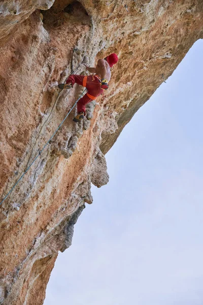 ロープとカービンで崖の端に登る赤い服の認識できないアルピニストの下のビューから — ストック写真