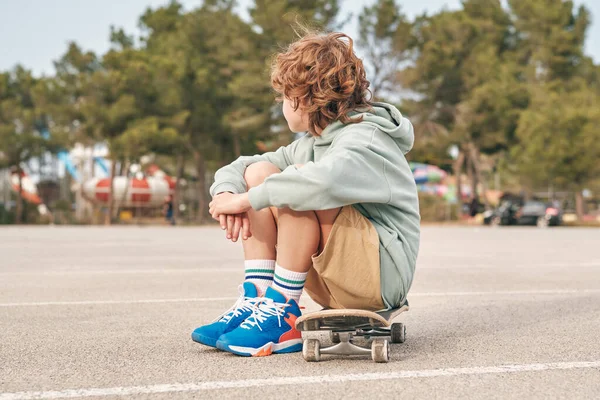 Боковой Вид Анонимного Подростка Крутом Костюме Сидящего Скейтборде Обнимающего Колени — стоковое фото