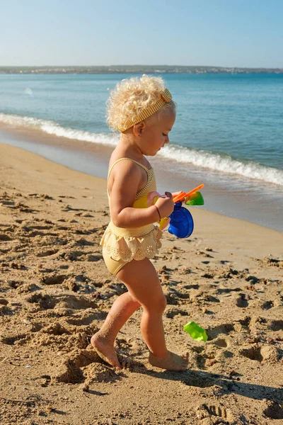 Side view of cute little girl playing with toys while spending time on sandy beach on sunny day