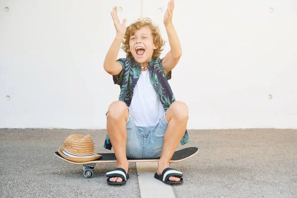 Aufgeregter Junge Freizeitkleidung Sitzt Auf Skateboard Gegen Weiße Wand Auf — Stockfoto