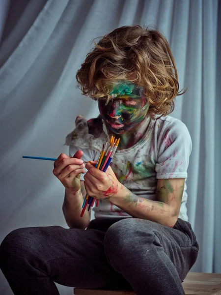 Zaostřený Špinavý Chlapec Pokrytý Barevnými Barvami Při Pohledu Sadu Štětců — Stock fotografie
