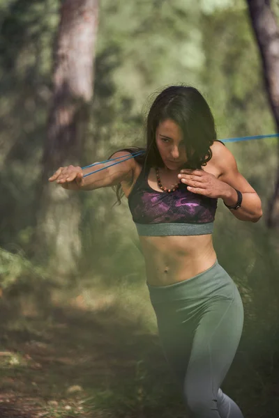严重的西班牙裔女性在树林中伸展手臂和锻炼背部肌肉时拉紧弹性带 — 图库照片