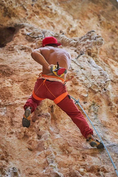 赤い服を着て崖の上に登ったり登ったりする無顔の運動強い男性の背中の景色 — ストック写真