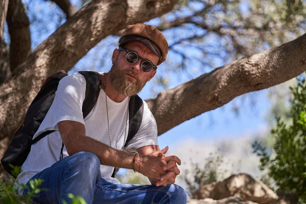 Low Angle Serious Male Tourist Sunglasses Backpack Sitting Tree Branch — Stock Photo, Image